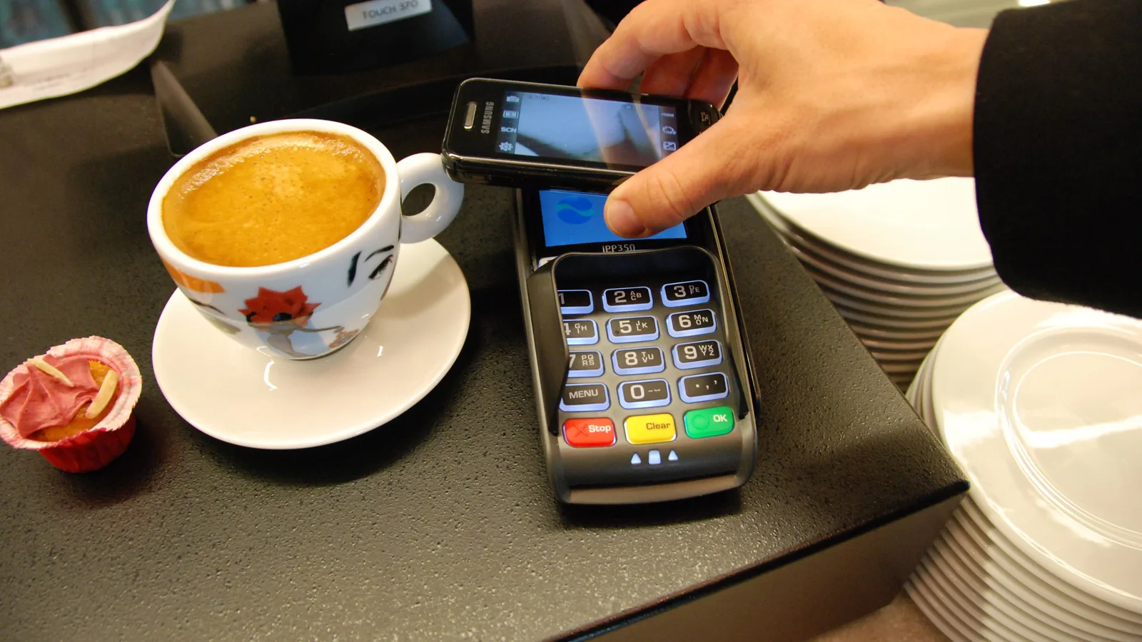 Customer tapping a smartphone on a contactless card terminal to pay at a café counter
