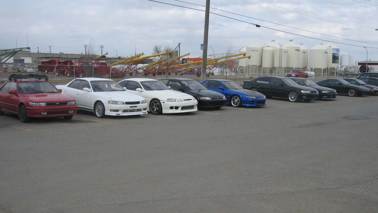 A row of used cars lined up for sale on a dealer lot, the inventory a dealer management system tracks