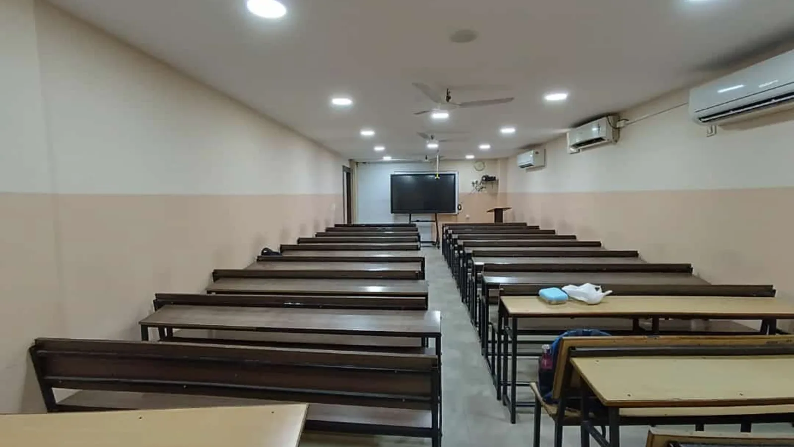 Empty coaching classroom in India with rows of benches and a digital display board
