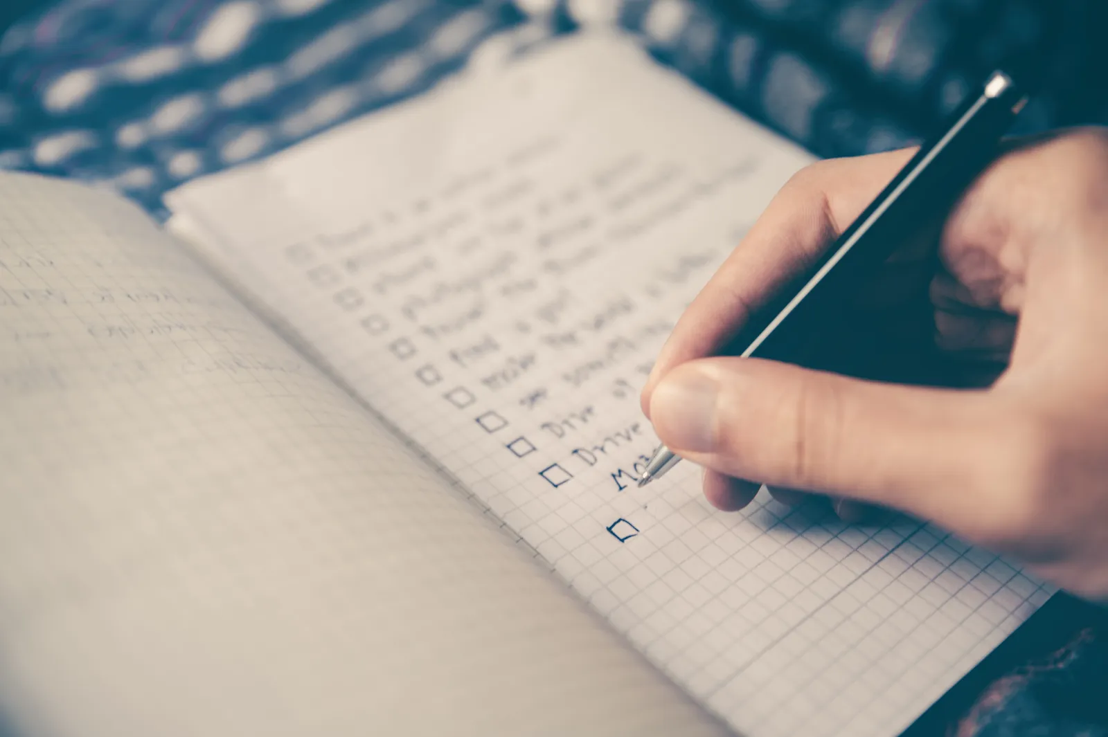 A hand writing a checklist with tick boxes in a grid-paper notebook