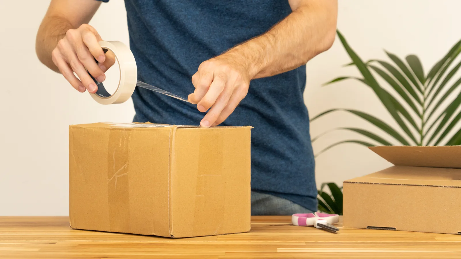 Seller sealing a cardboard box with packing tape to ship an online order