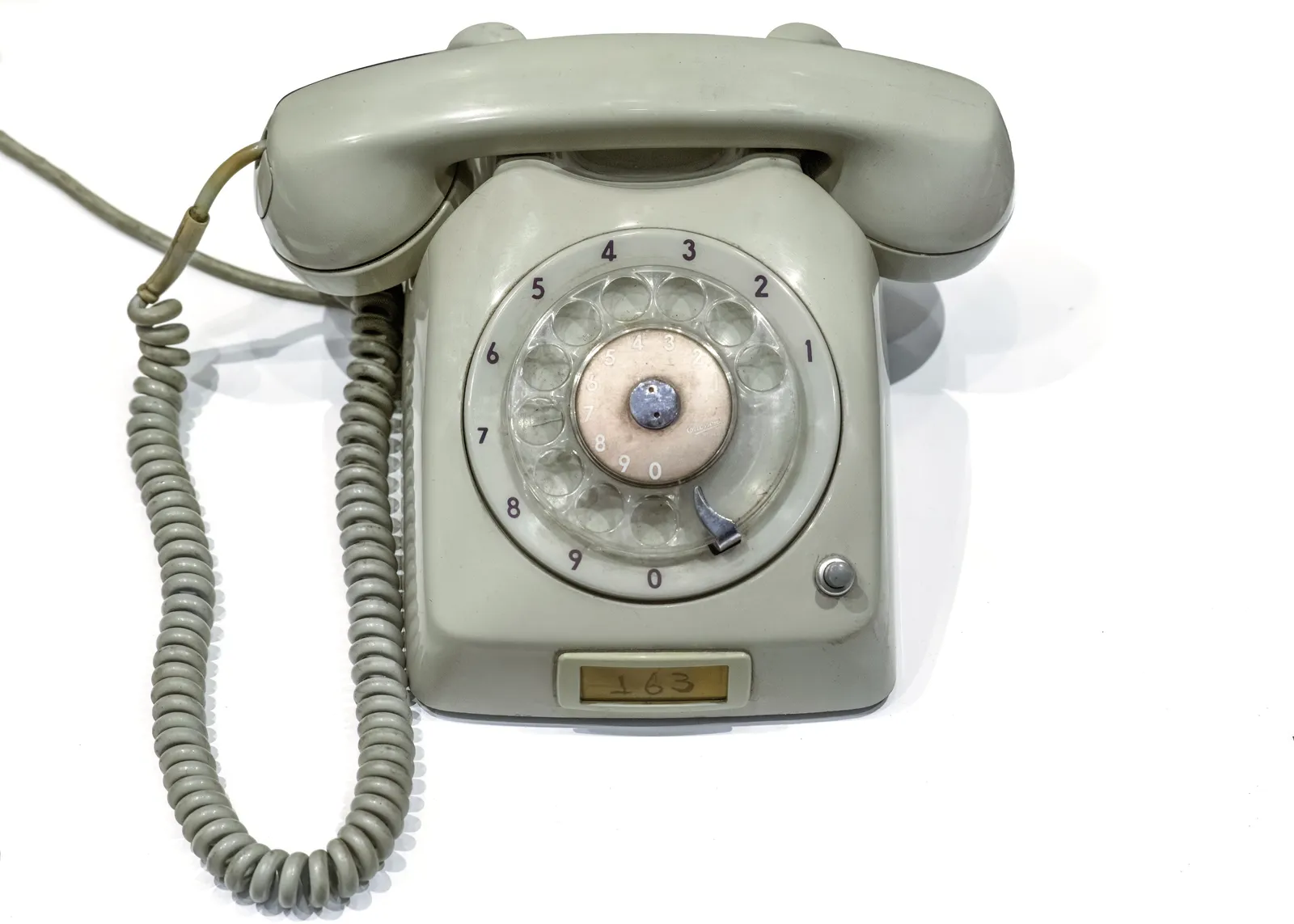Grey rotary-dial desk telephone with a coiled handset cord on a white background