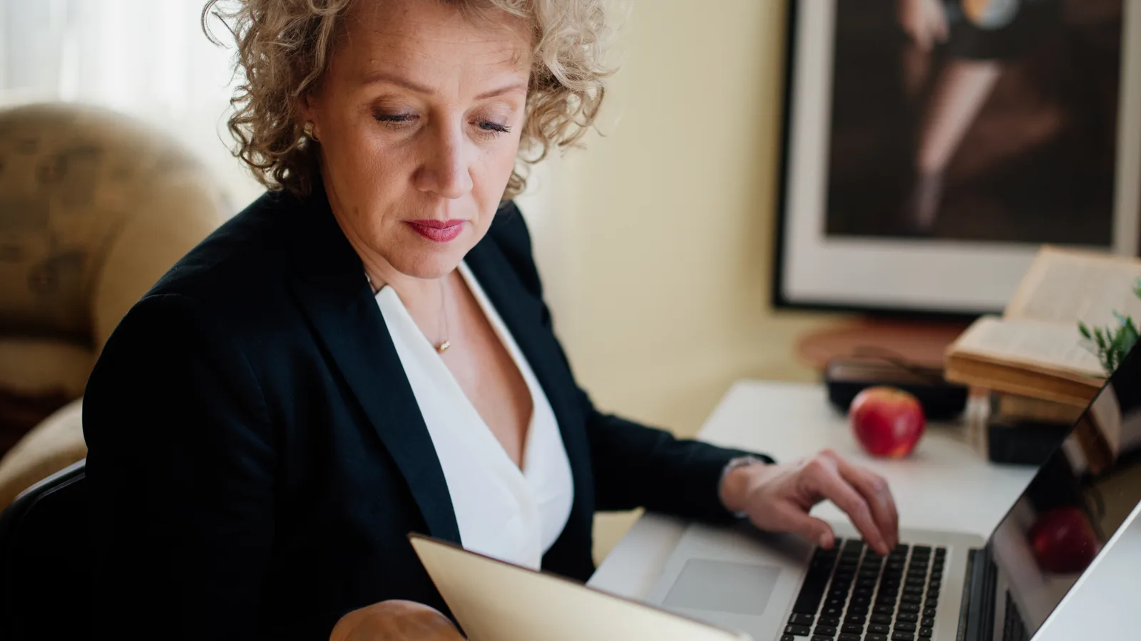 Sales professional reviewing documents and working on a laptop at her desk
